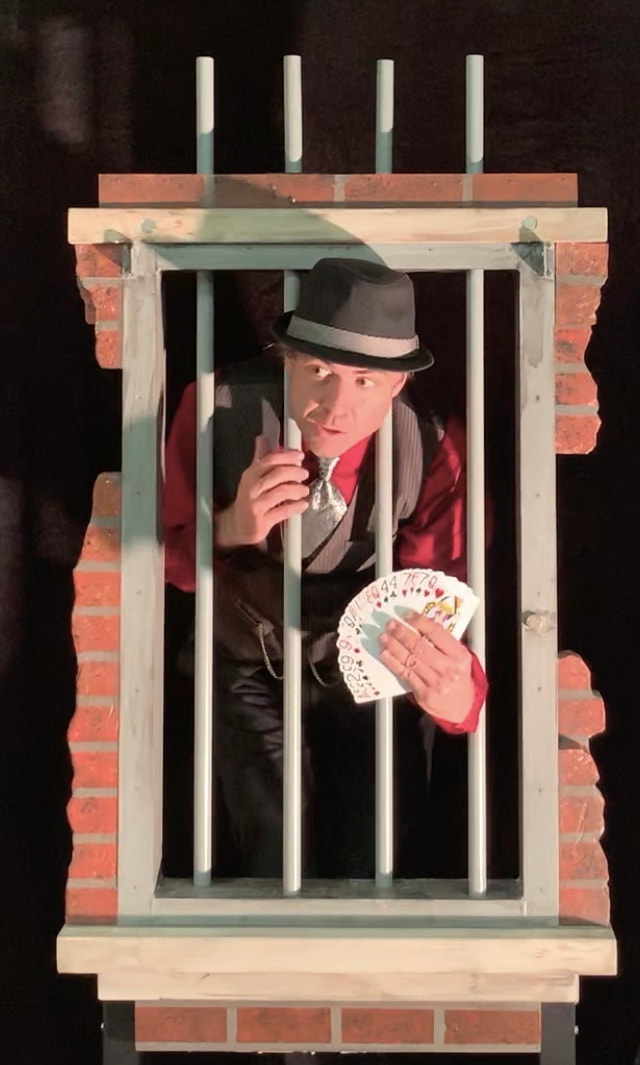 Illusionist holding playing cards through a jail cell window. 