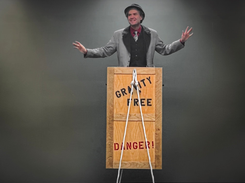 Illusionist levitating while standing inside a wooden crate with white ropes tethering it to the ground. "Gravity Free Danger!" is written on the wooden box. 